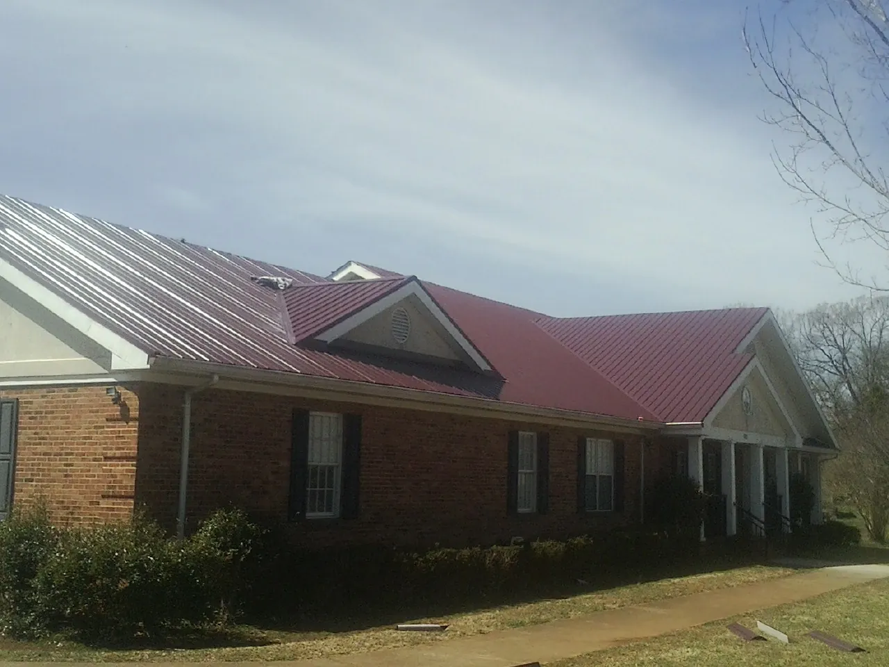 Red metal roof with gabled entries on a long brick building, from a Hail Damage Roof Repair job in Le Sueur