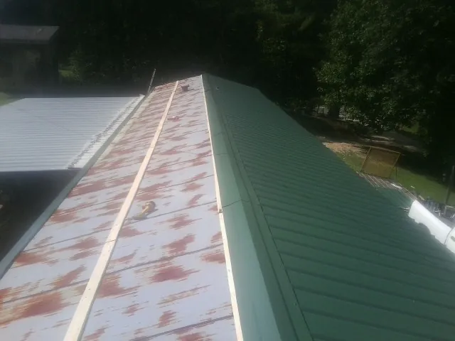 Old rusted panels beside newly installed green metal roofing — Wind Damage Roof Repair by Roofing Brothers in Le Sueur