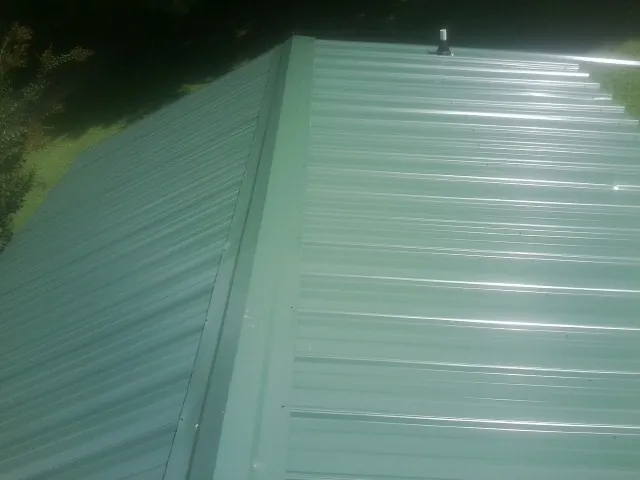 New green metal panels meeting at the ridge of a roof — Flat Roof Repair work by our crew in Le Sueur