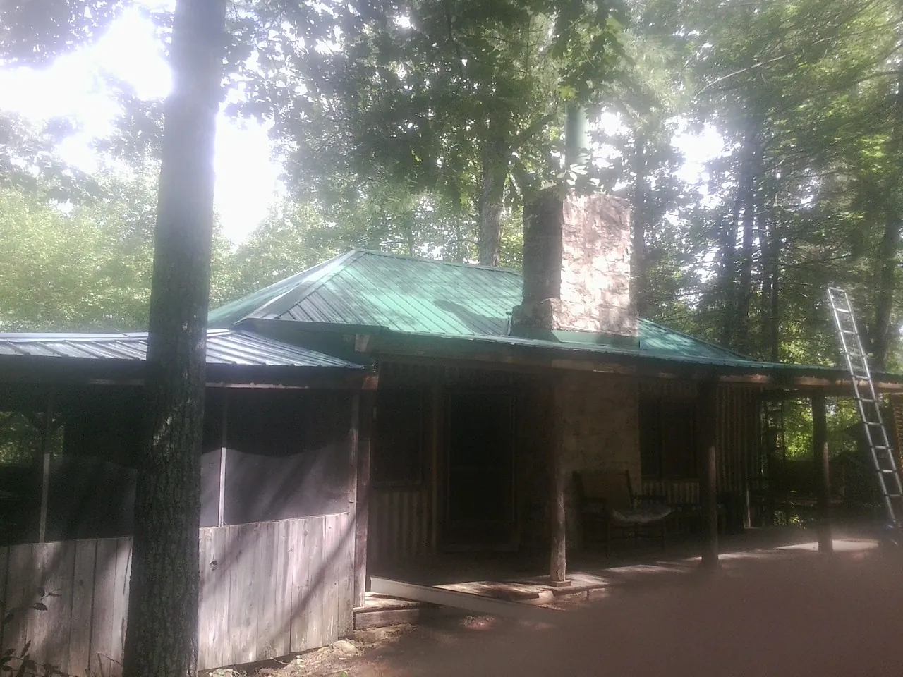 Green metal roof and stone chimney above a log cabin porch in Le Sueur