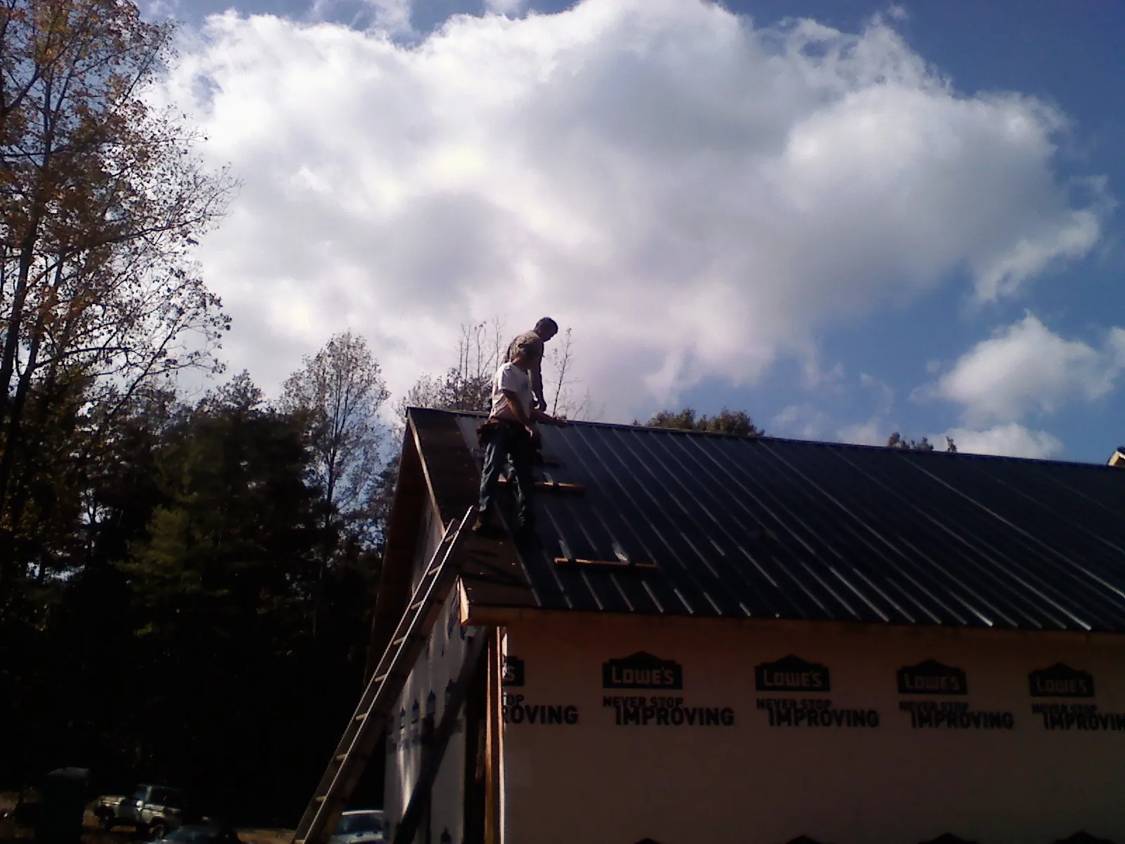 Roofer fastening dark metal panels high against a cloudy sky, from a Roof Inspection job in Le Sueur