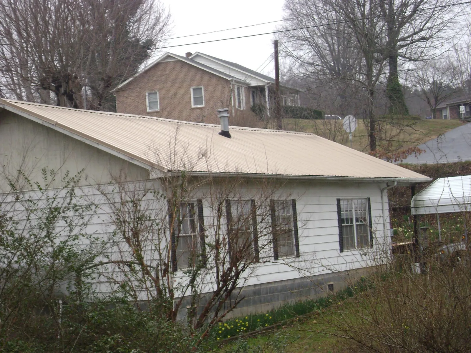 Tan metal roof on a white sided house set into a hillside — Commercial Roofing by Roofing Brothers in Le Sueur