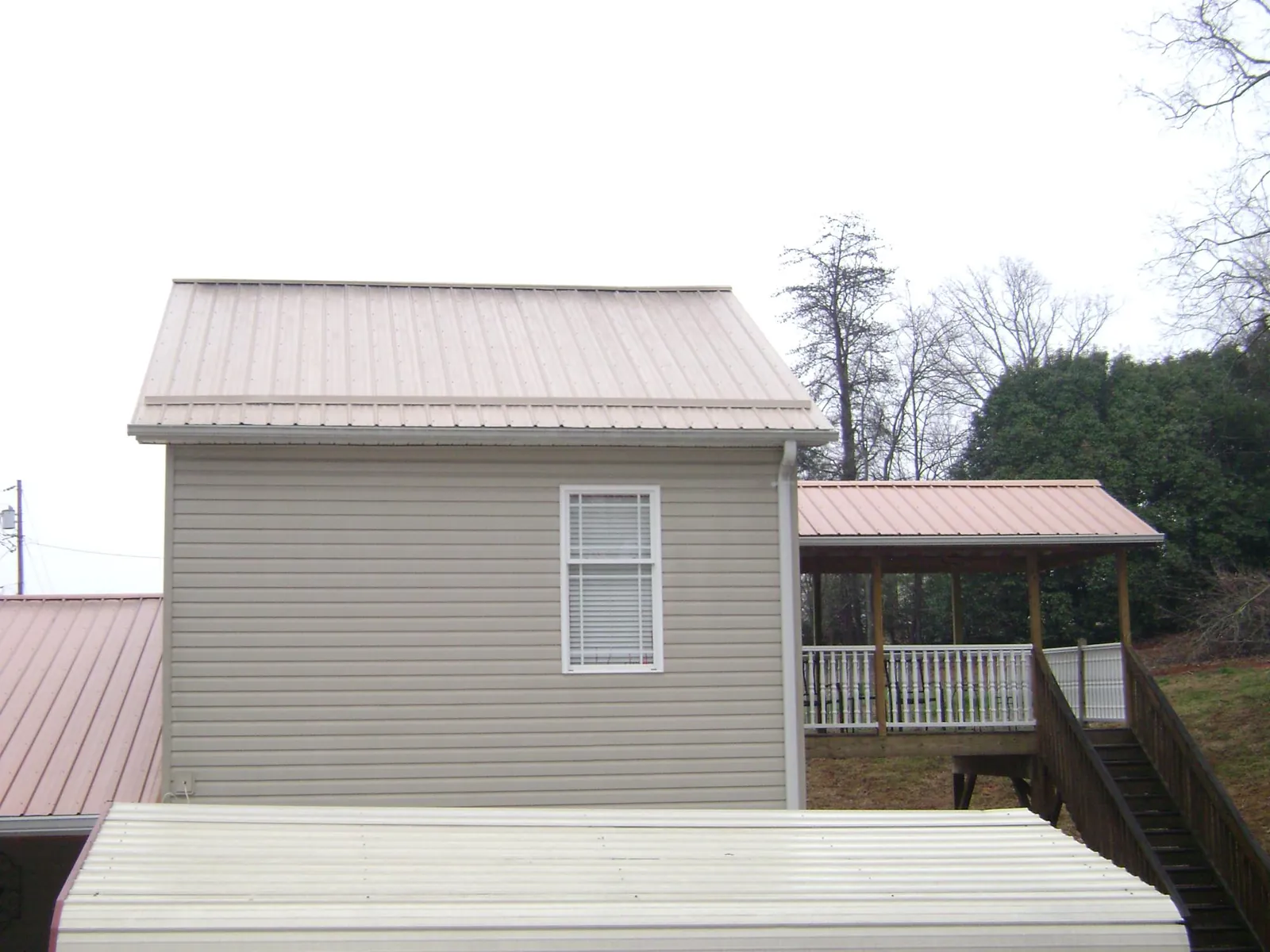 Tan metal roofs on a two story addition and attached porch, from a Roof Replacement job in Le Sueur